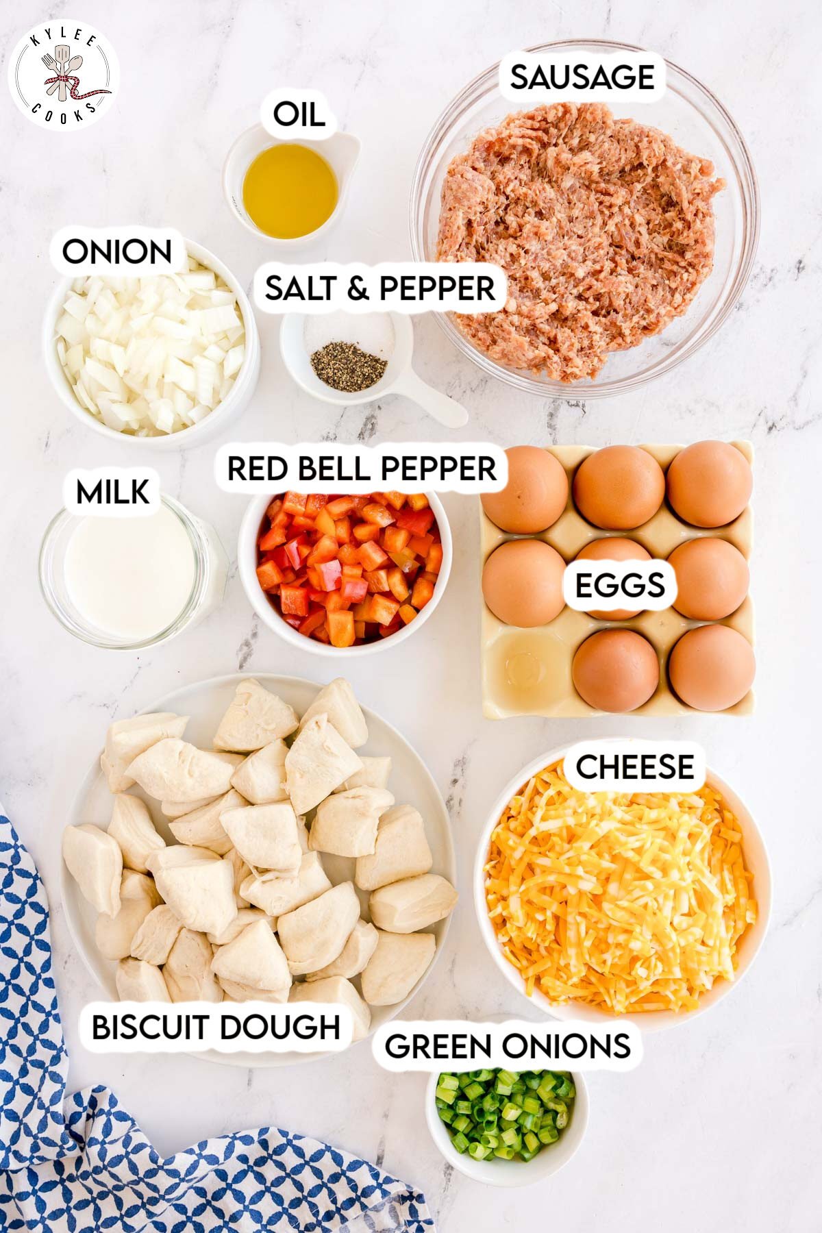 Measured ingredients for biscuit breakfast bake labeled on the image, including sausage, eggs, cheese, red bell pepper, onion, green onions, milk, flour, oil, and salt & pepper. Text on the image says each ingredient name.
