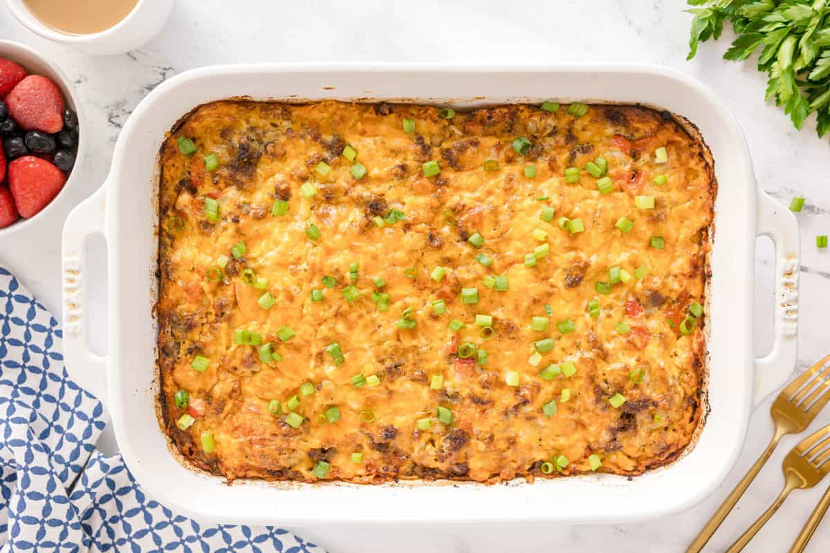 A baked biscuit breakfast casserole in a white dish topped with melted cheese and chopped green onions.