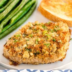 A plate with a blue cheese crusted pork chop, green beans, and toasted bread.
