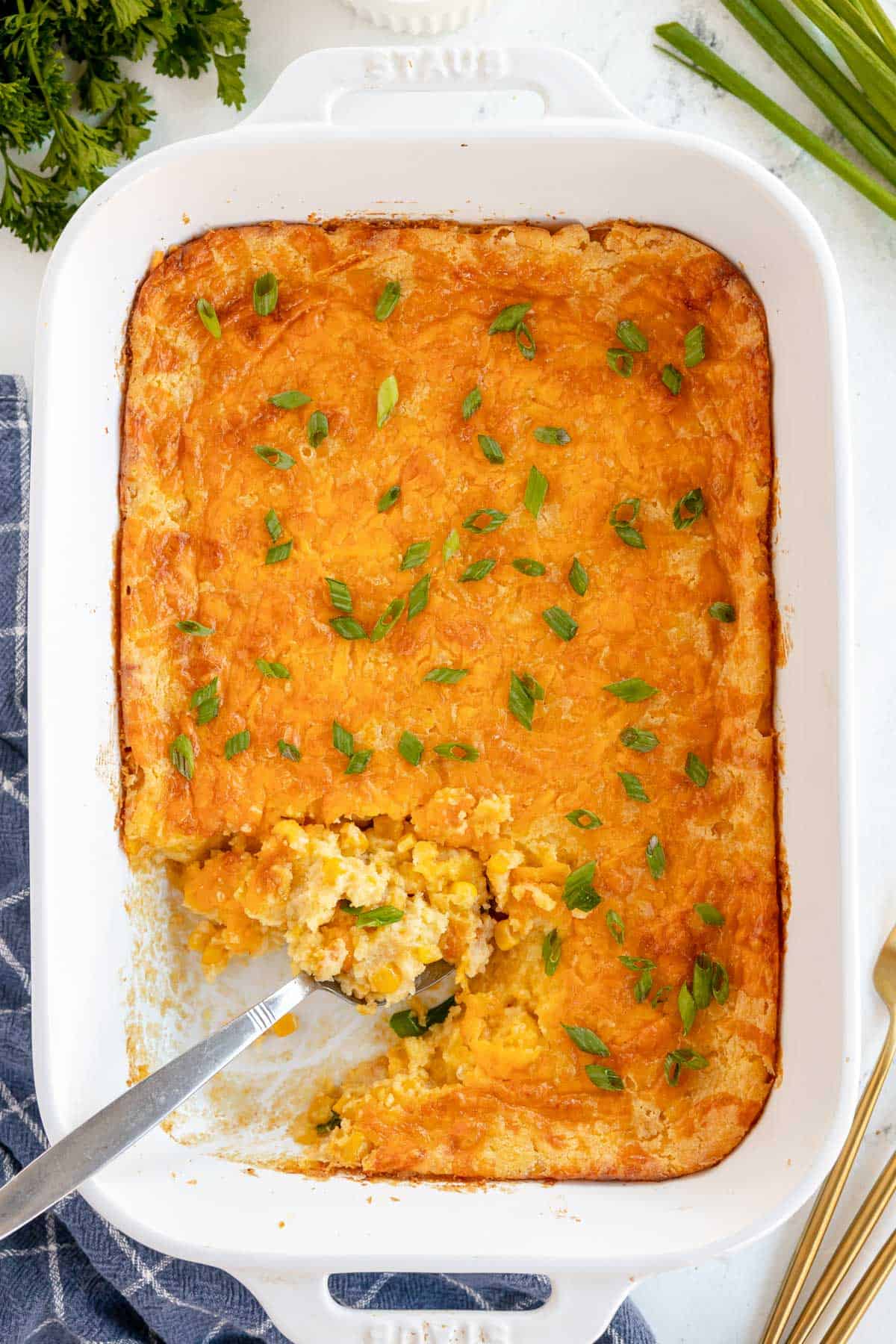 Cheesy corn casserole in a white dish with a spoon.