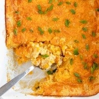 Cheesy corn casserole in a white dish with a spoon.