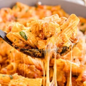 A spoonful of rigatoni with chicken, marinara sauce, and melted cheese being lifted from the pan.