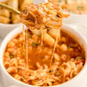 A spoonful of cheesy chicken parmesan soup held above a white bowl, with melted cheese stretching from the spoon.