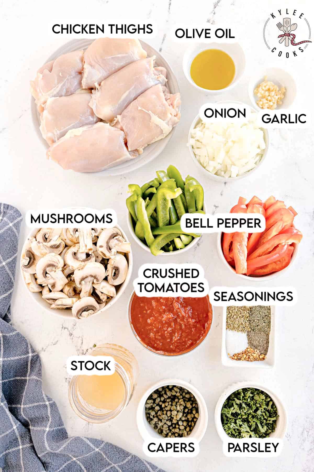 A top-down view of ingredients for crockpot chicken cacciatore, including raw chicken thighs, mushrooms, bell peppers, onion, garlic, crushed tomatoes, chicken broth, olive oil, capers, parsley, and seasonings, with labels on each ingredient.