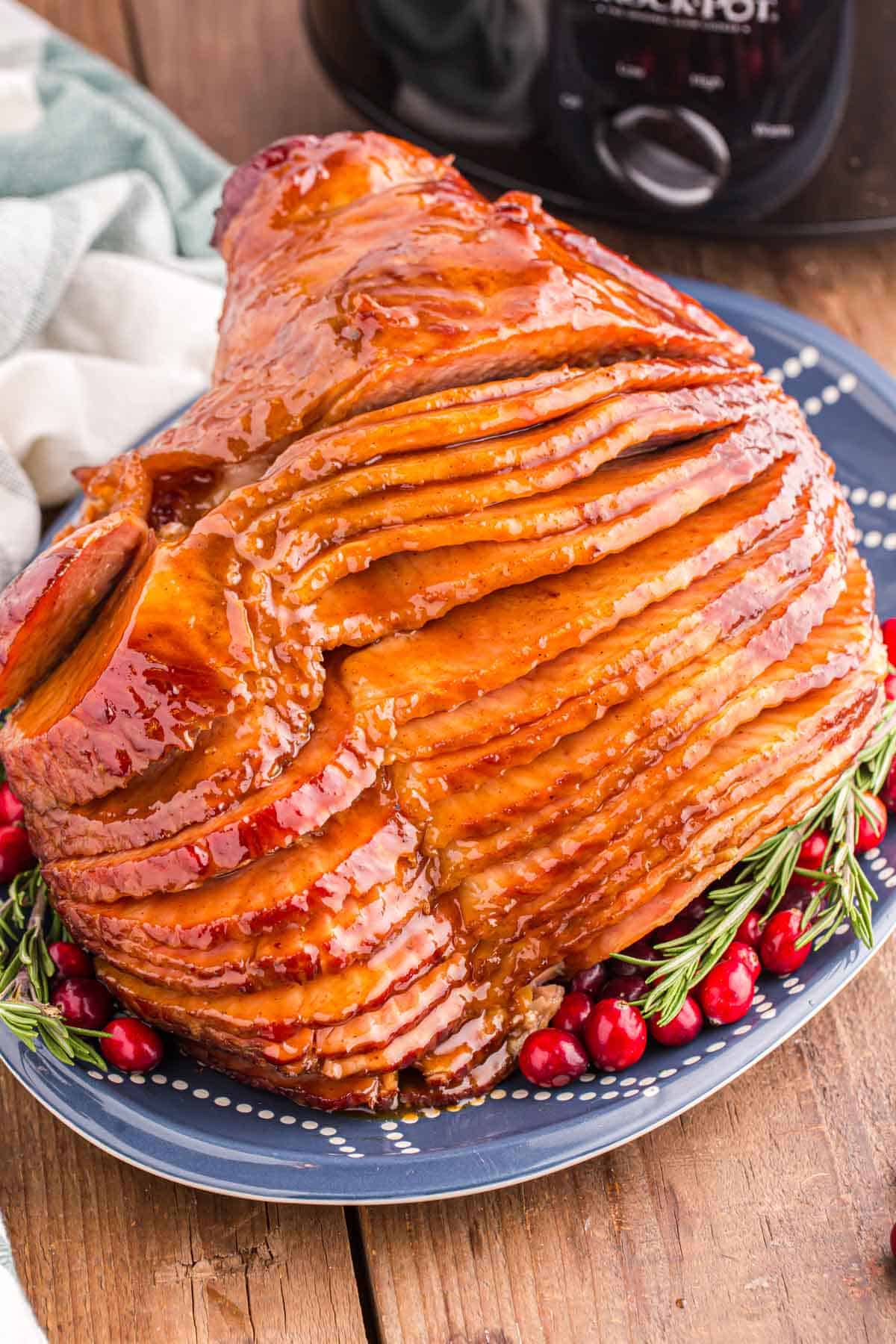 Sliced glazed ham garnished with fresh rosemary sprigs on a blue plate.