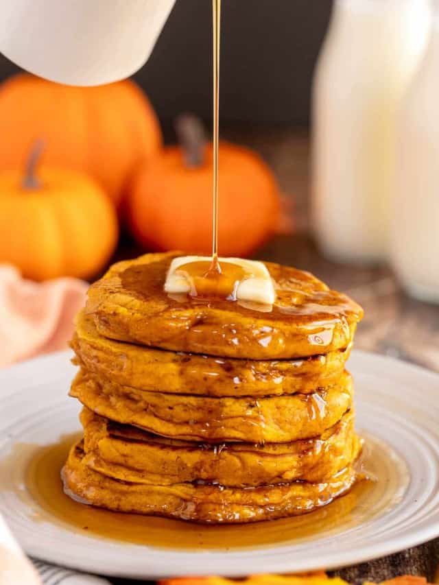 Pumpkin spice pancakes being drizzled with maple syrup.