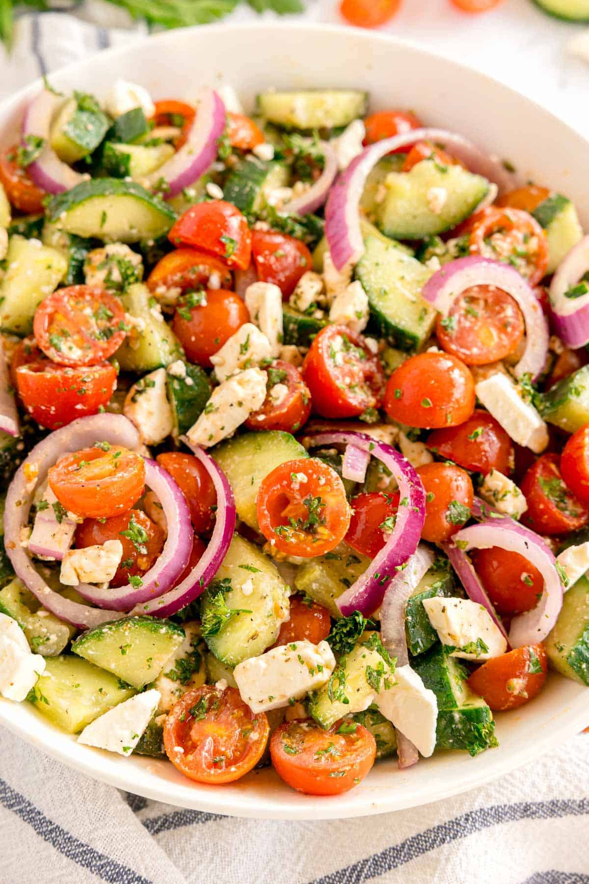 A close-up of chopped cucumber, tomatoes, red onion, and feta in a bowl.