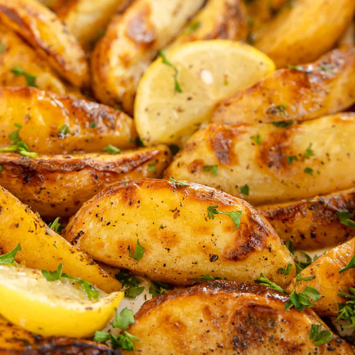 Close-up of seasoned and roasted potato wedges garnished with fresh parsley and lemon slices.