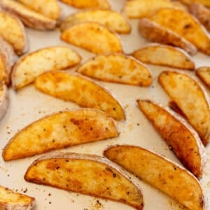 Baked potato wedges on a sheet pan, golden and crisp with seasoning.