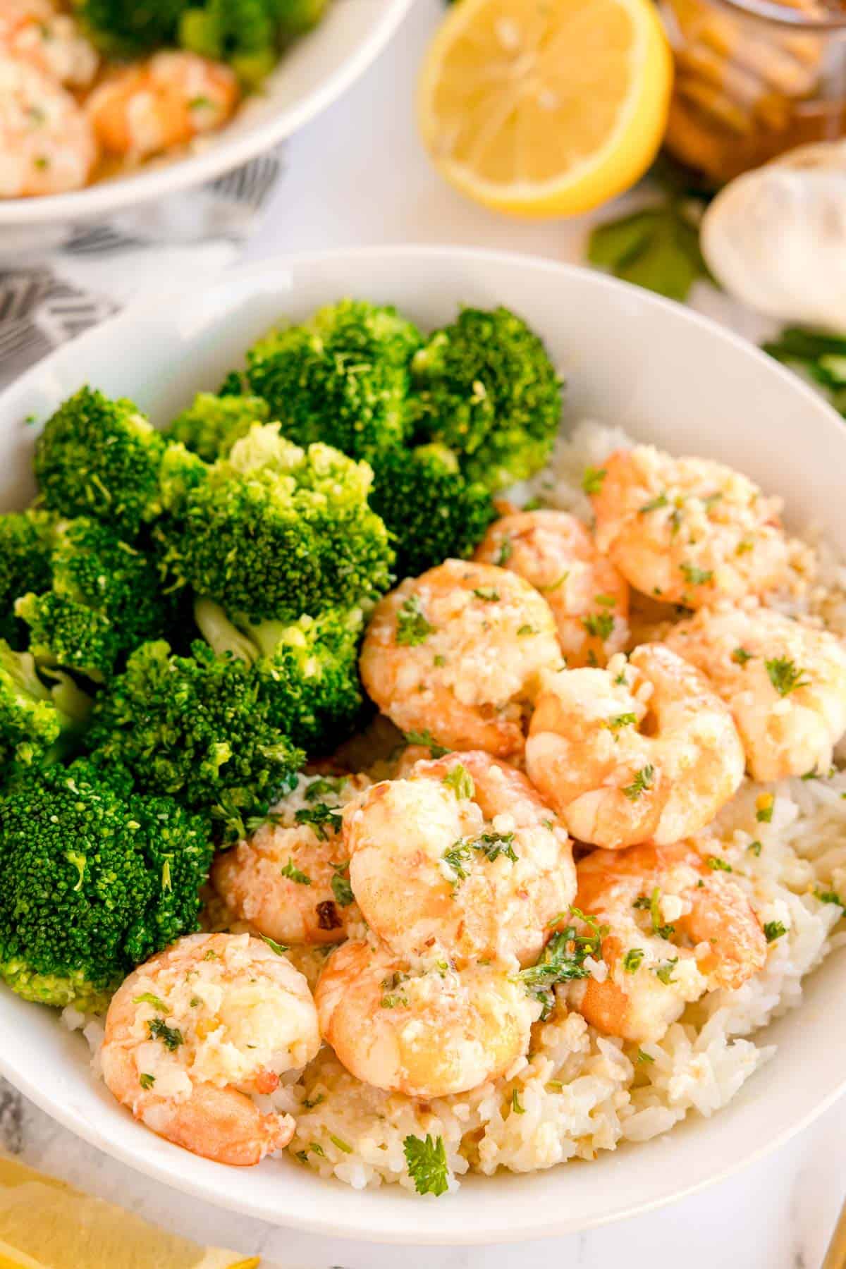A bowl with shrimp, broccoli, and rice. A lemon and garlic are nearby.