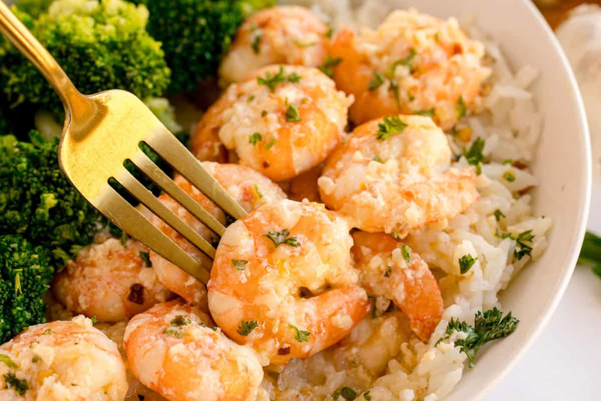 A fork picking up shrimp from a bowl of rice and broccoli.