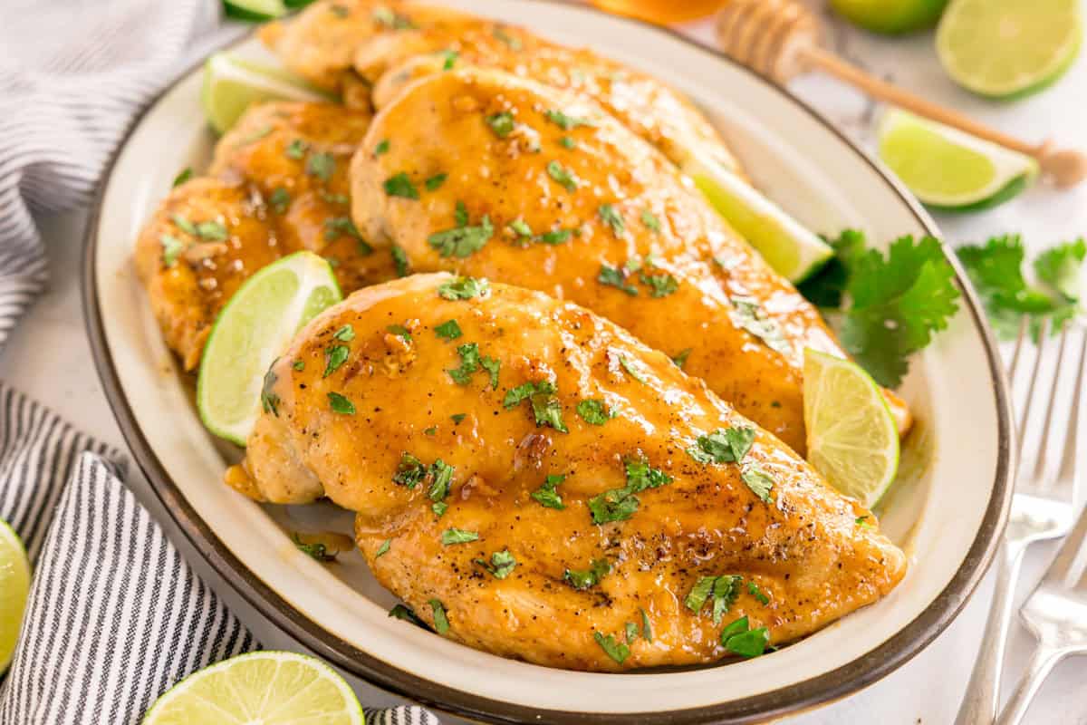 Glazed chicken on a serving plate with lime wedges and sprinkled cilantro.
