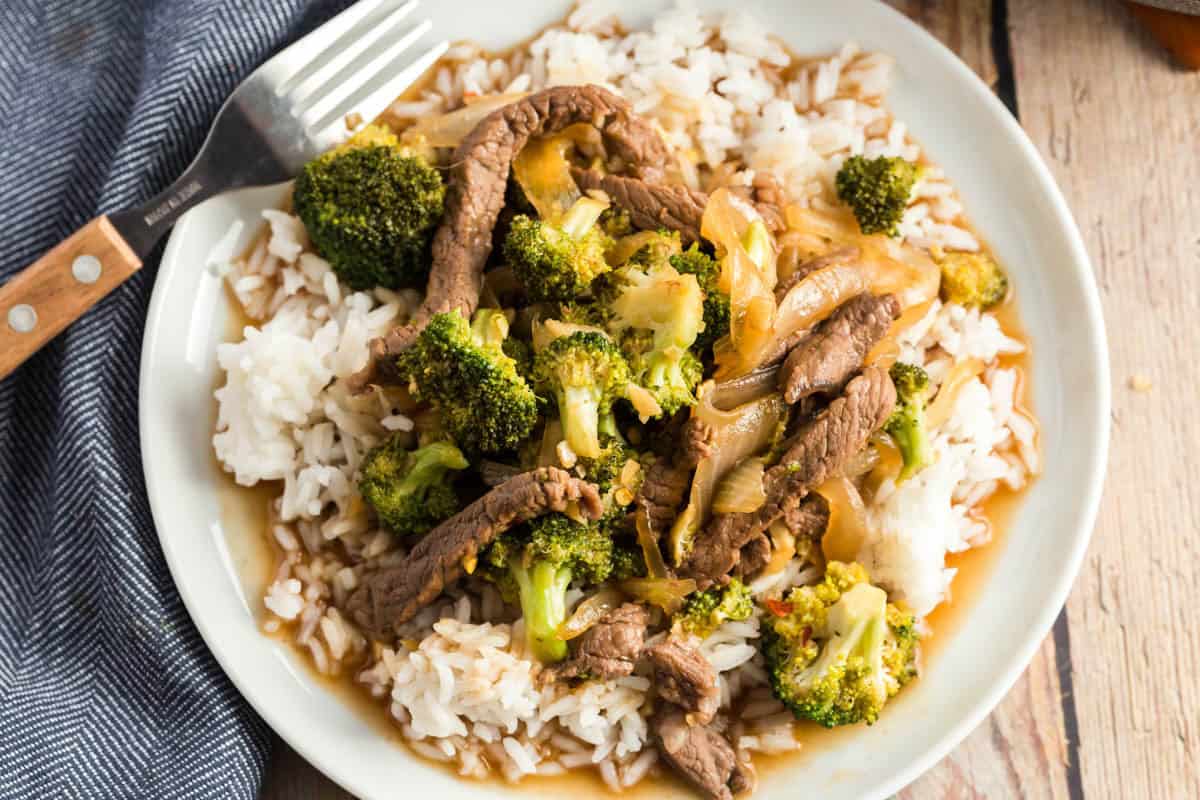 A plate of honey soy beef and broccoli served over white rice, with a fork resting on the side.
