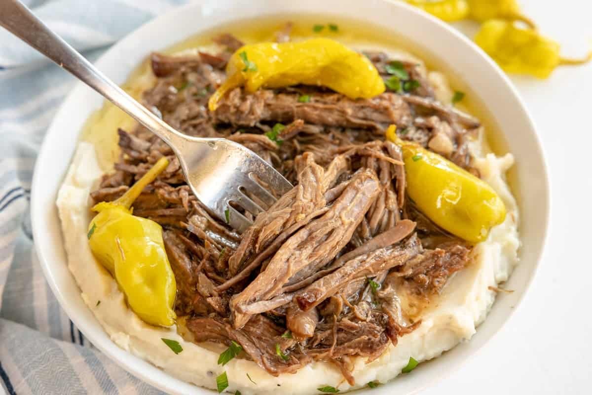 A bowl of pot roast on mashed potatoes, garnished with herbs and a fork.