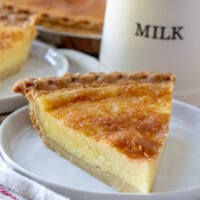 A slice of Buttermilk Pie on a white plate with a jug labeled "MILK" in the background.