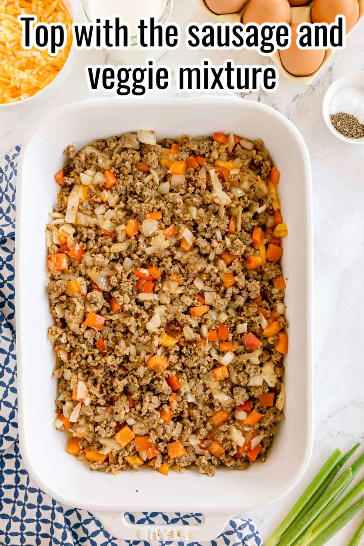 Sausage and veggie mixture layered over biscuit dough in a baking dish. Text on the image says 'Top with the sausage and veggie mixture'.