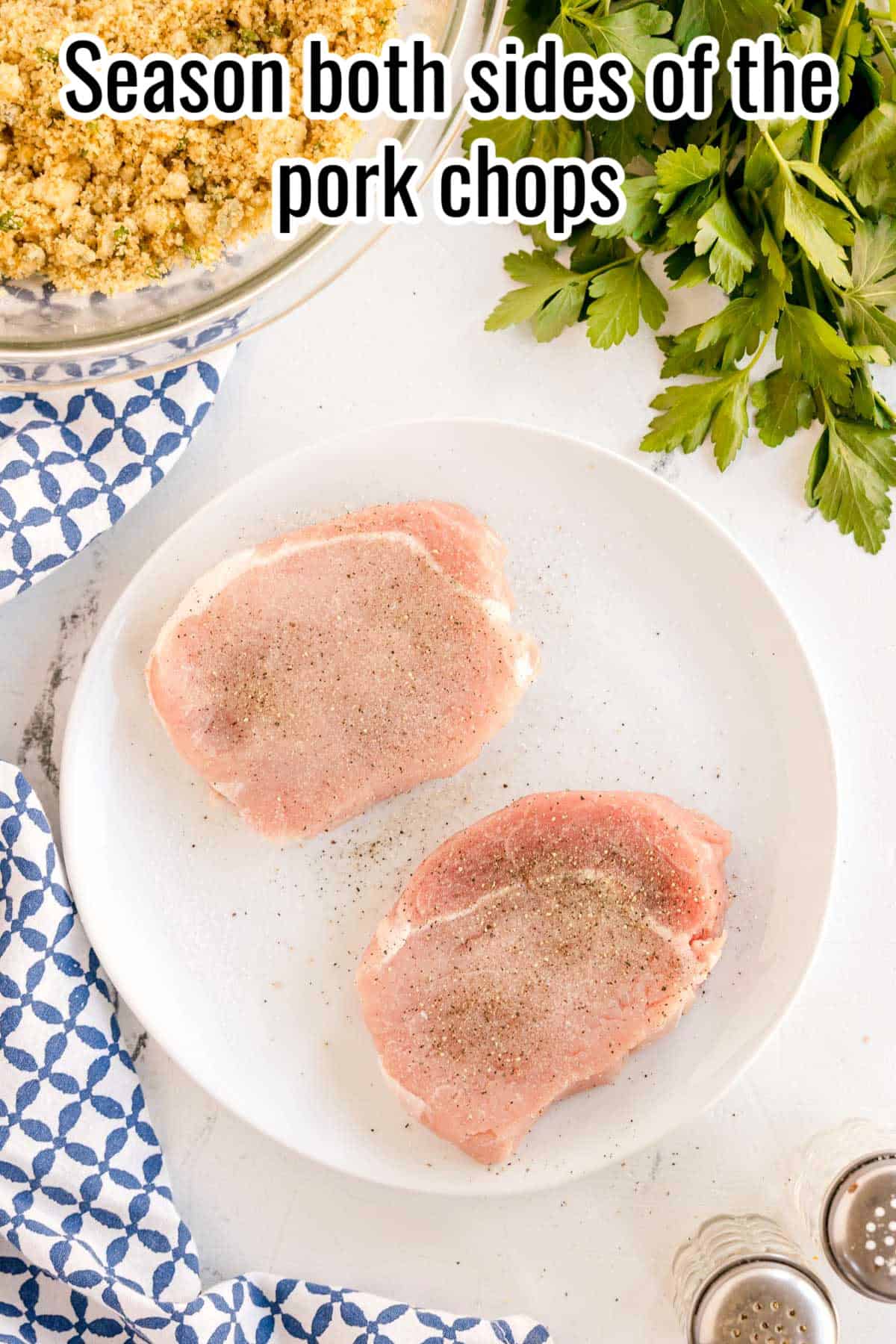 Two raw pork chops on a plate, sprinkled with salt and pepper. Text on the image says 'Season both sides of the pork chops'.