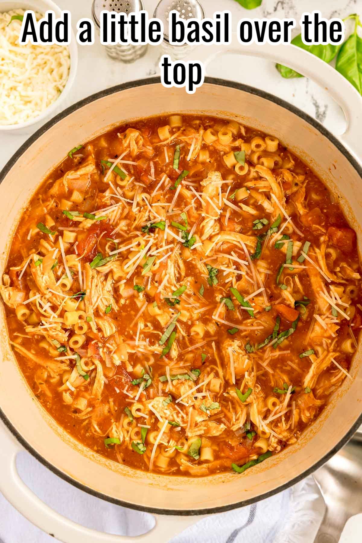 Chicken parmesan soup topped with shredded parmesan and chopped basil. Text on the image says 'Add a little basil over the top'.