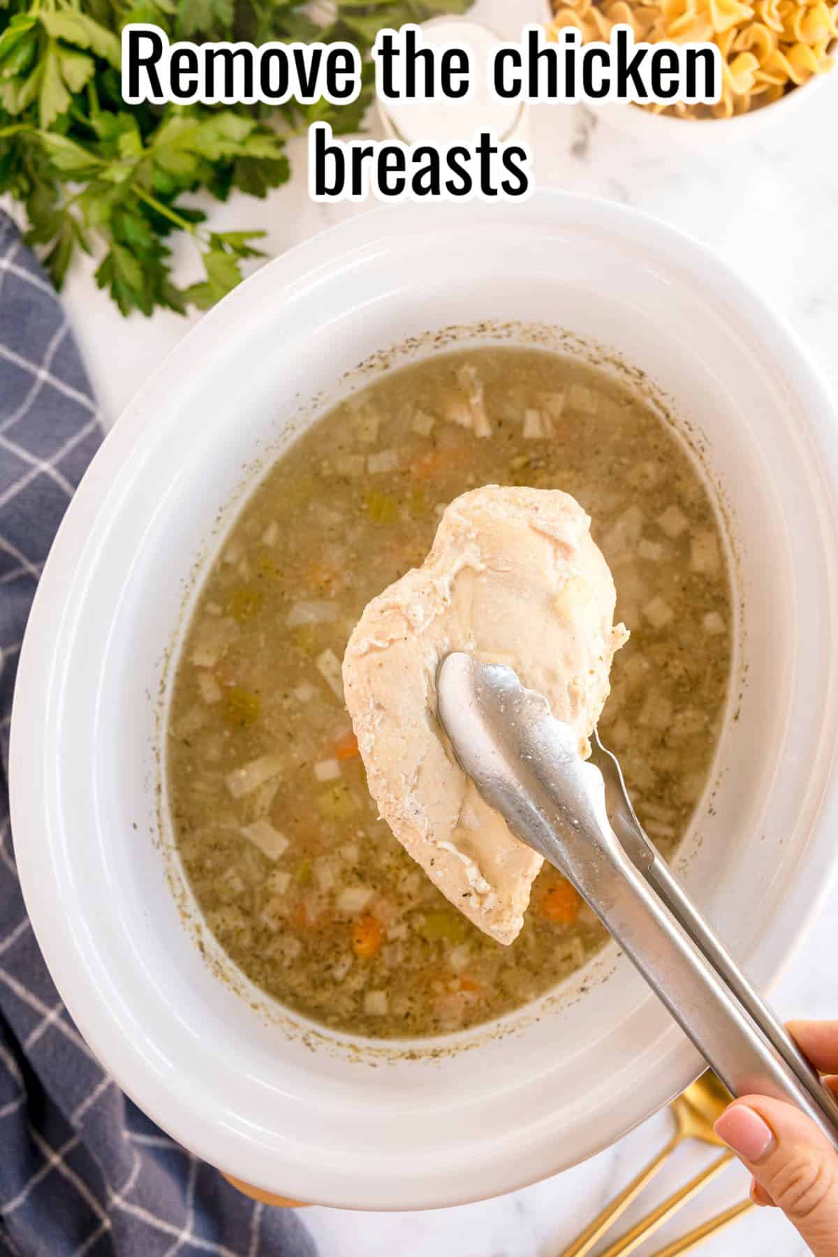 A cooked chicken breast being lifted from broth in the slow cooker with tongs. Text on the image says 'Remove the chicken breasts'.