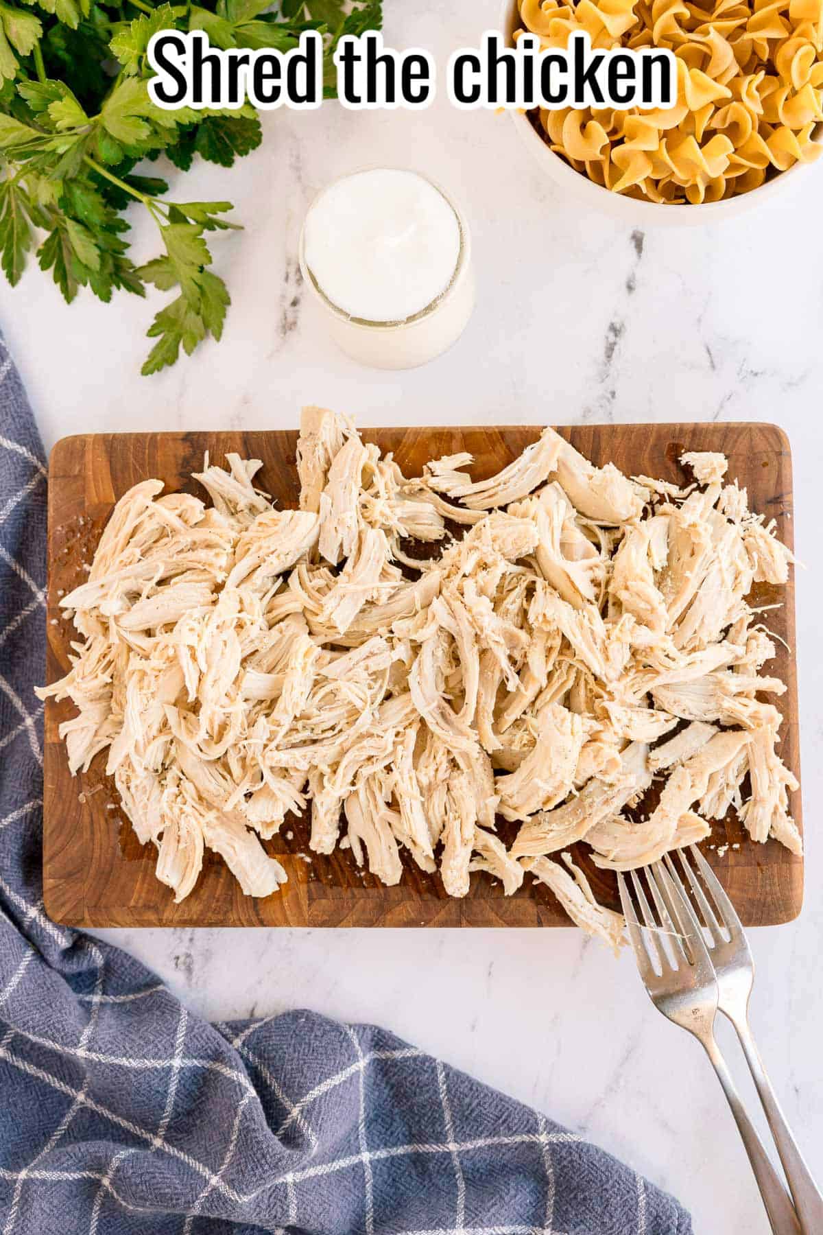Shredded chicken on a wooden cutting board with two forks. Text on the image says 'Shred the chicken'.