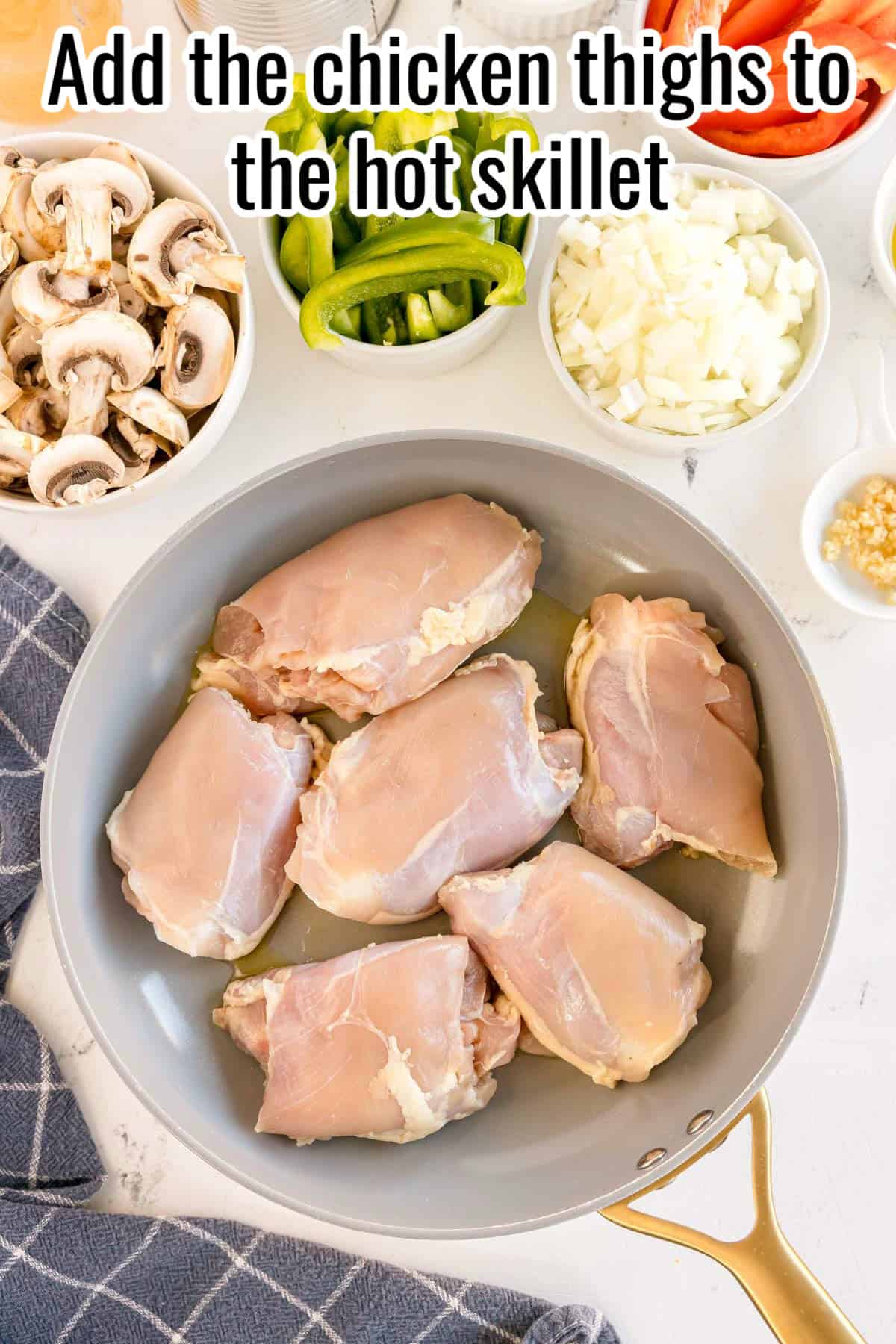 Raw chicken thighs placed in a skillet with a bit of oil, surrounded by bowls of sliced mushrooms, bell peppers, chopped onions, and minced garlic, with a text overlay that reads "Add the chicken thighs to the hot skillet."