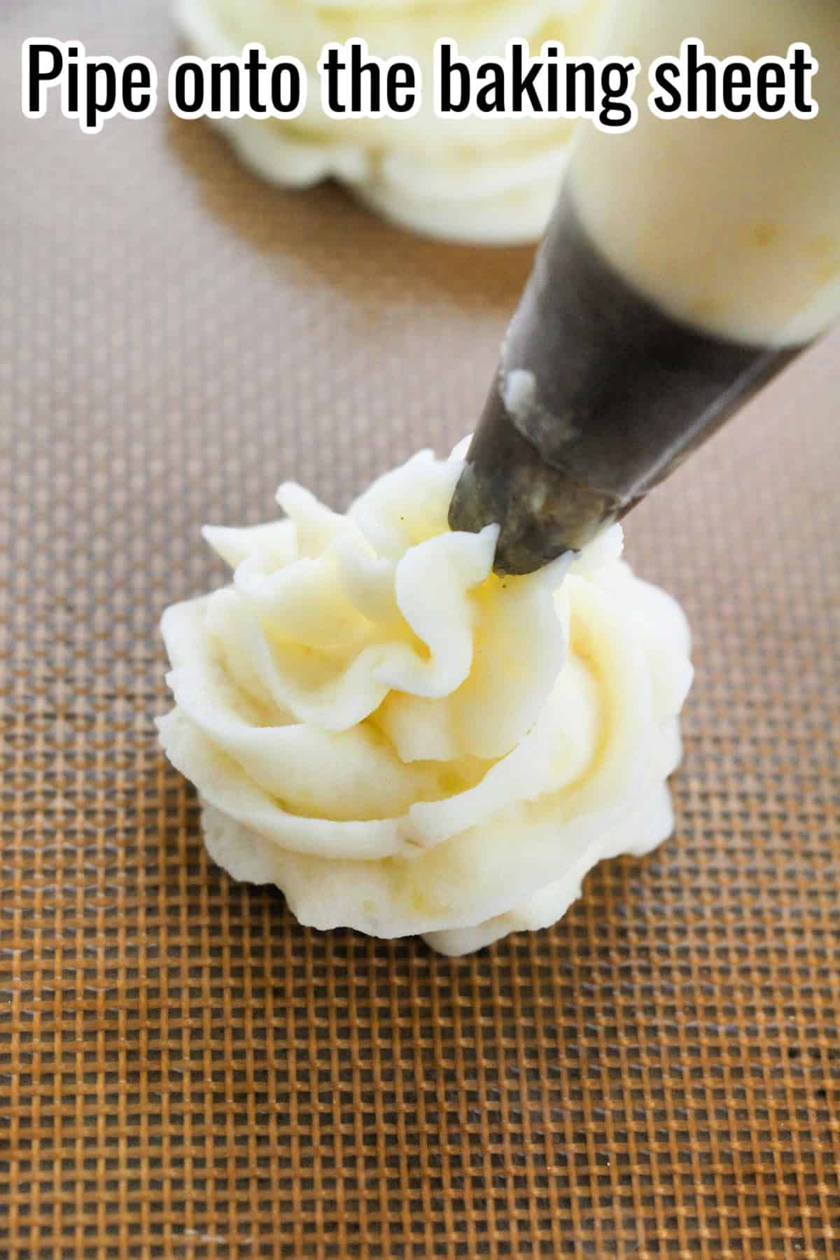A swirl of mashed potatoes being piped onto a baking mat. Text on the image says 'Pipe onto the baking sheet'.