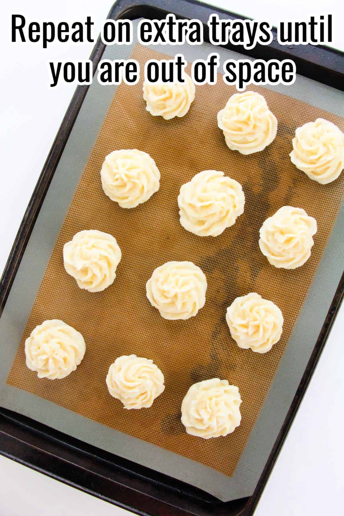 A baking tray with rows of piped duchess potatoes. Text on the image says 'Repeat on extra trays until you are out of space'.