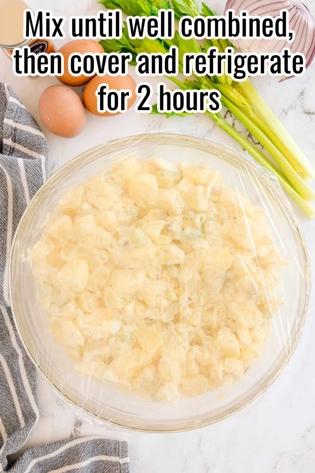 A bowl of potato salad covered with plastic wrap. Text on the image says 'Mix until well combined, then cover and refrigerate for 2 hours'.