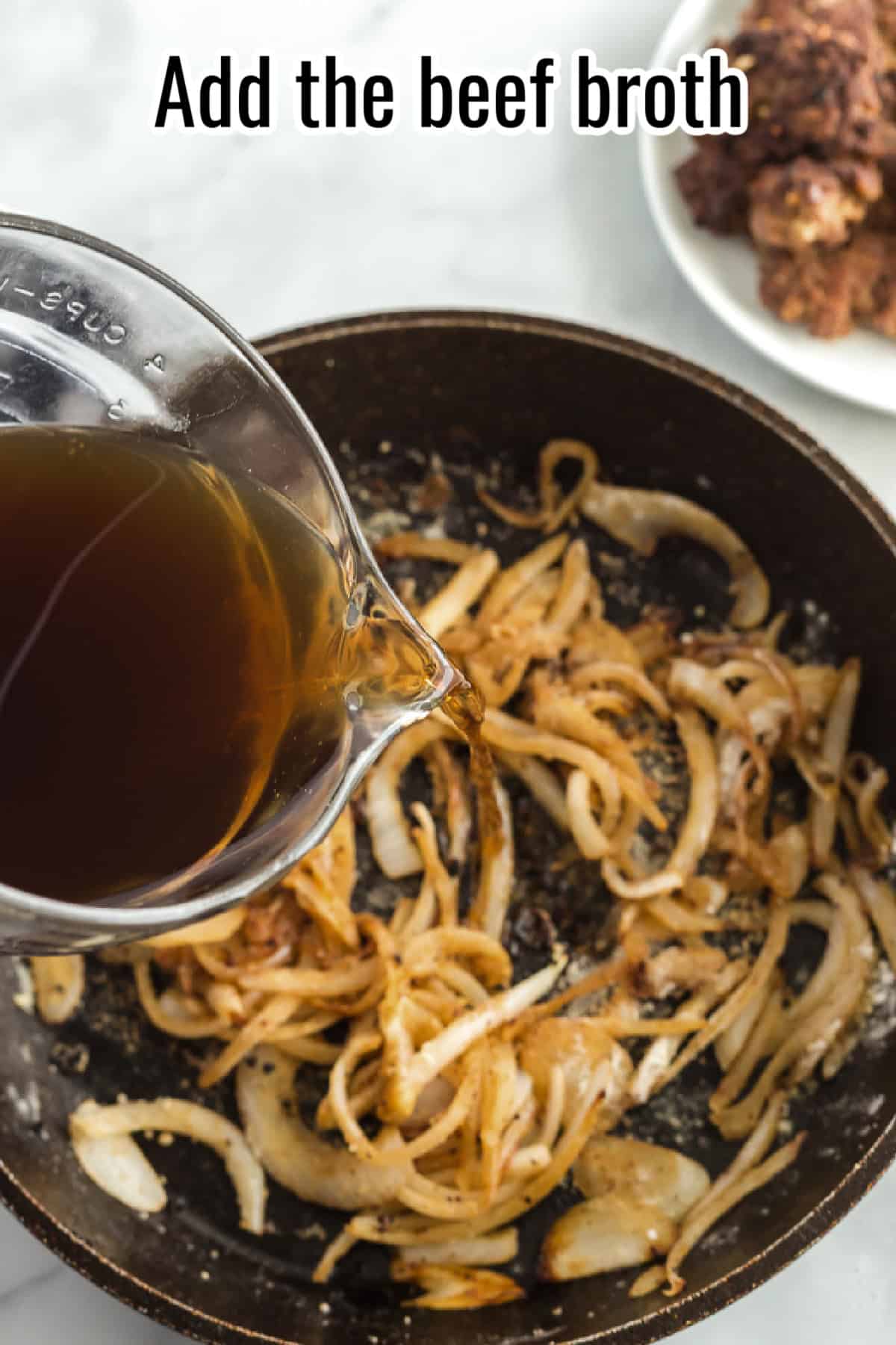 A measuring cup pouring beef broth into a skillet with cooked onions, with text overlay reading "Add the beef broth."