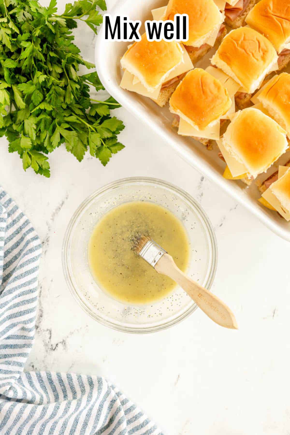 A dish of ham and cheese sliders with a bowl of parsley.