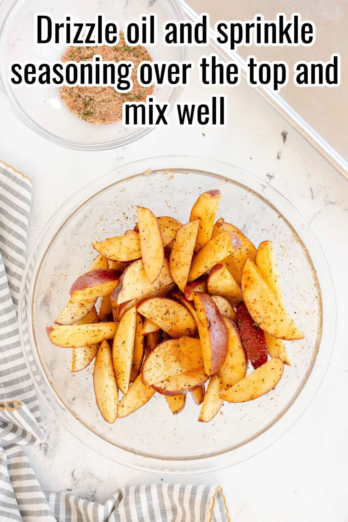 Potato wedges in a bowl coated with seasoning. Text on the image says 'Drizzle oil and sprinkle seasoning over the top and mix well'