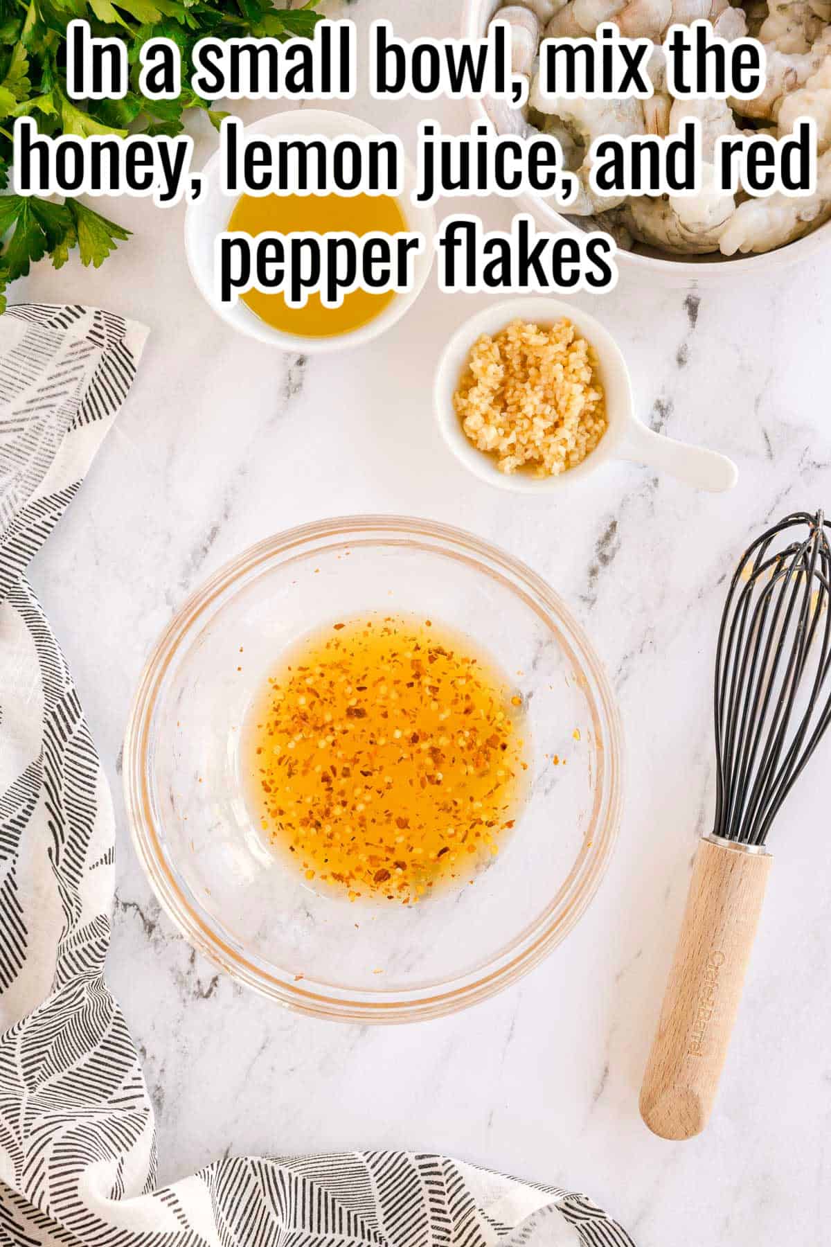 A glass bowl with a honey, lemon juice, and red pepper flakes mixture. Garlic, shrimp, and ingredients are nearby. Text on the image says 'In a small bowl, mix the honey, lemon juice, and red pepper flakes'.