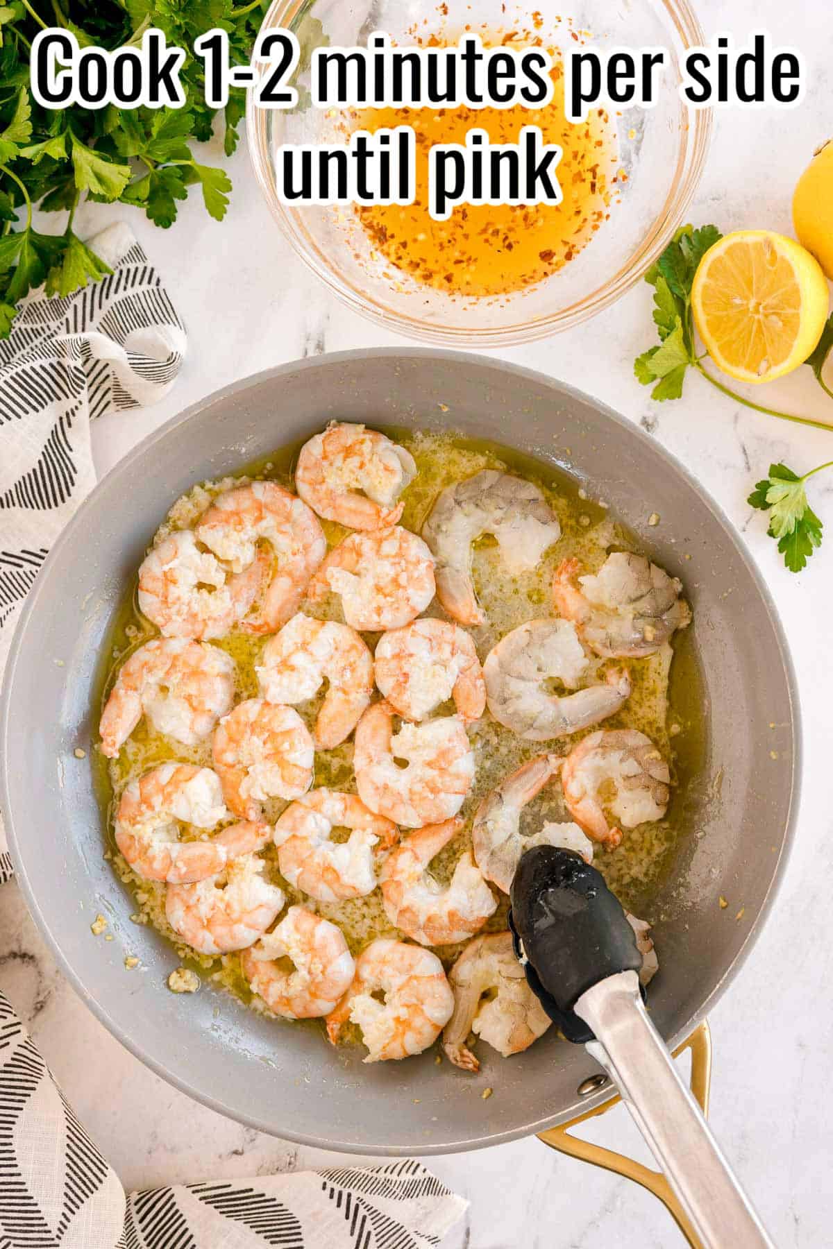 Shrimp turning pink while cooking in the pan. A pair of tongs is turning one. Text on the image says 'Cook 1-2 minutes per side until pink'.