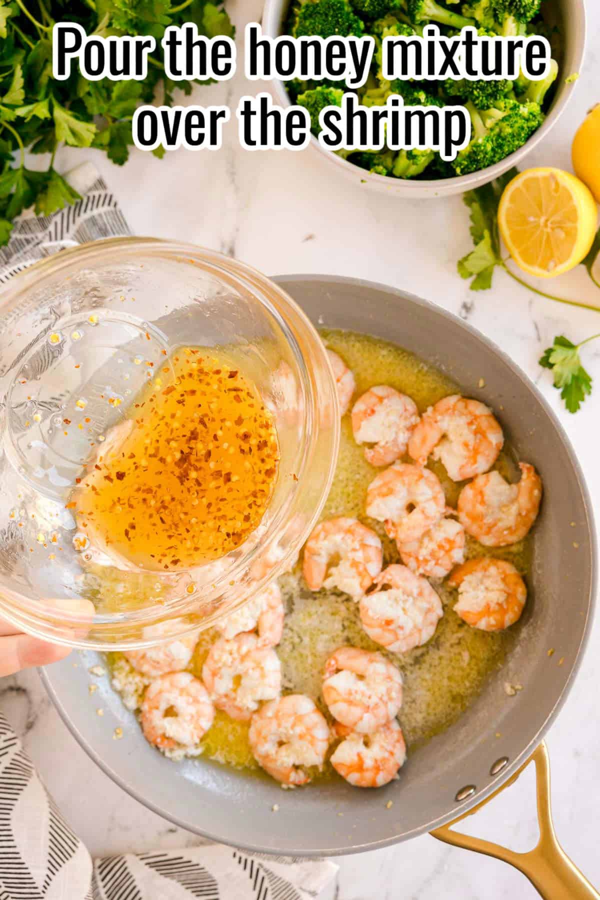 A hand pouring the honey mixture into the pan of cooked shrimp. Text on the image says 'Pour the honey mixture over the shrimp'.