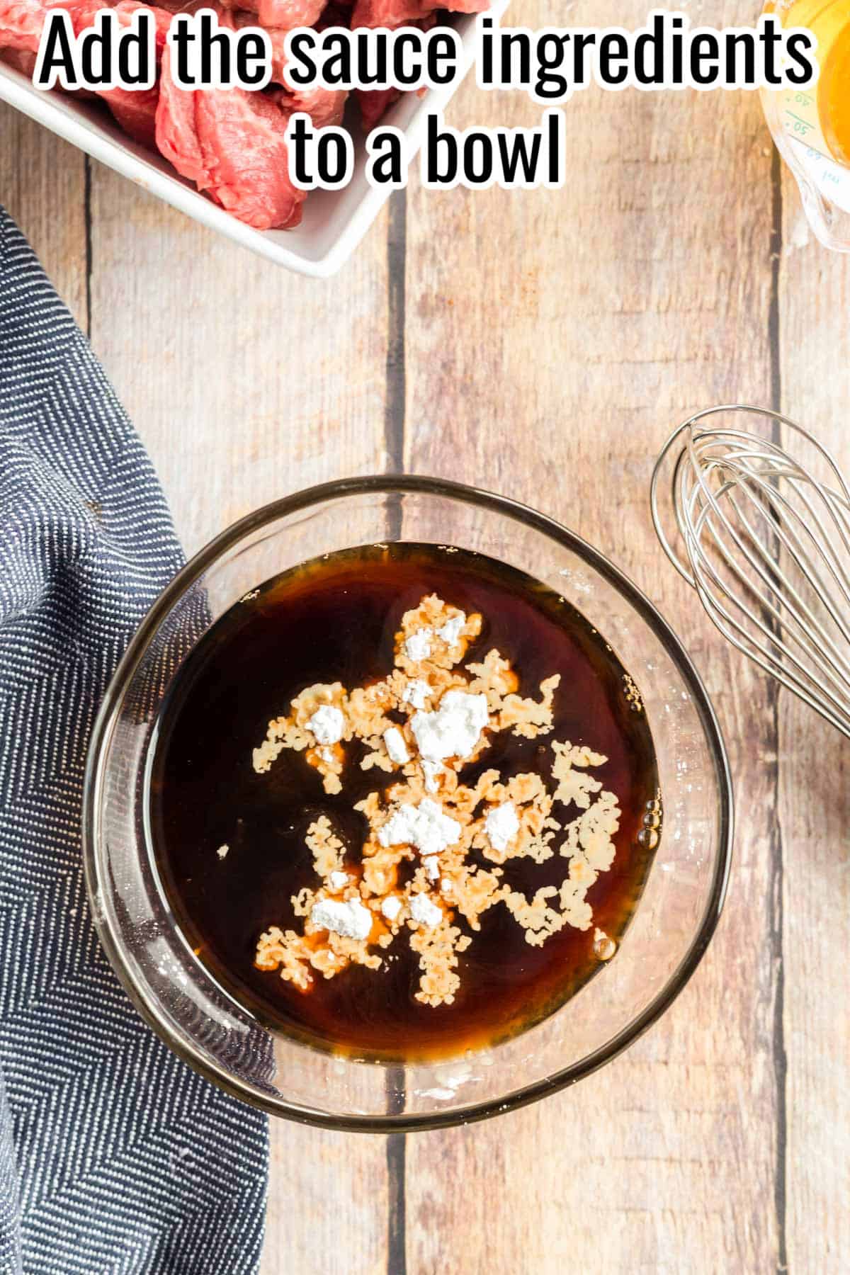 A glass bowl with dark soy sauce mixture, cornstarch, and garlic, ready to be whisked, with raw beef and a whisk nearby. Text on the image says 'Add the sauce ingredients to a bowl'.