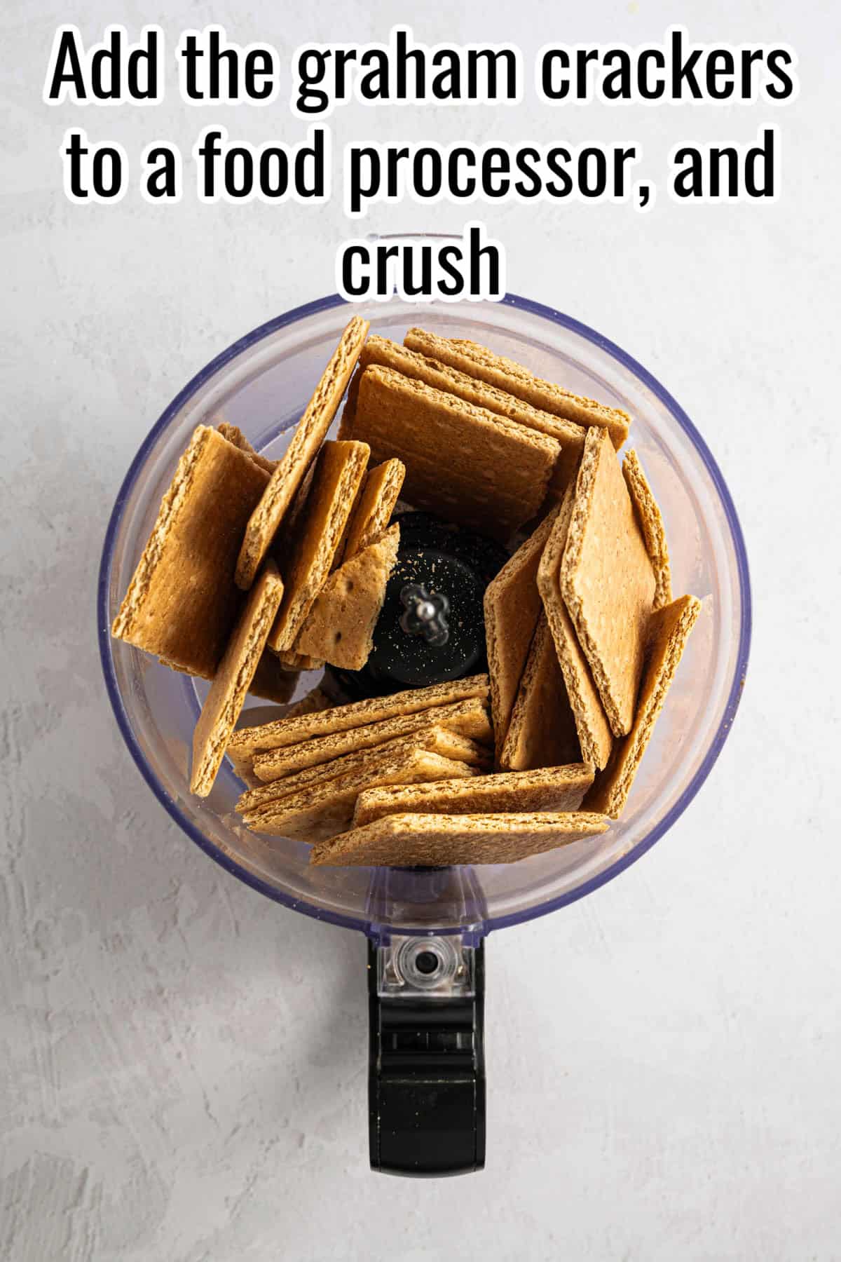 A food processor filled with graham crackers, ready to be crushed. Text on the image says 'Add the graham crackers to a food processor, and crush'.