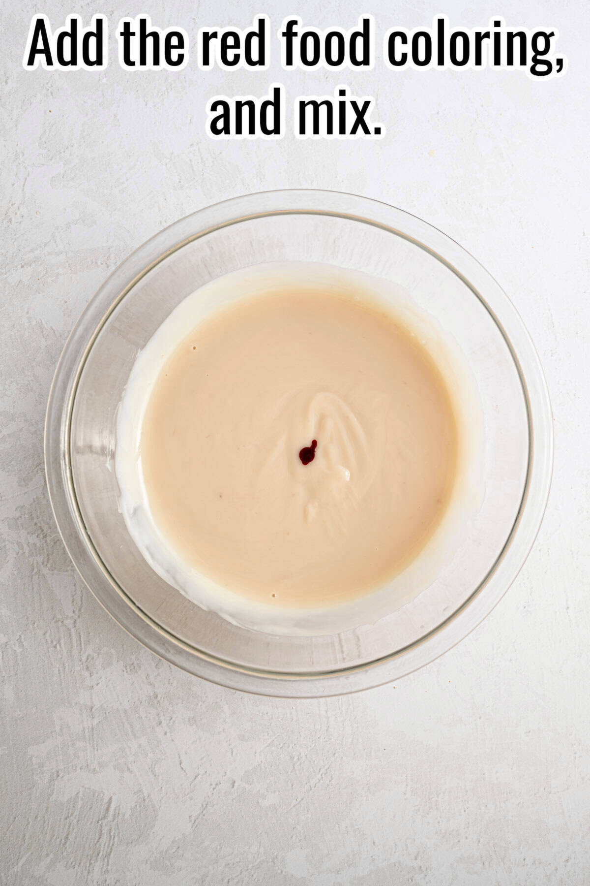 A bowl with the red food coloring dot in a creamy mixture. Text on the image says 'Add the red food coloring, and mix'.