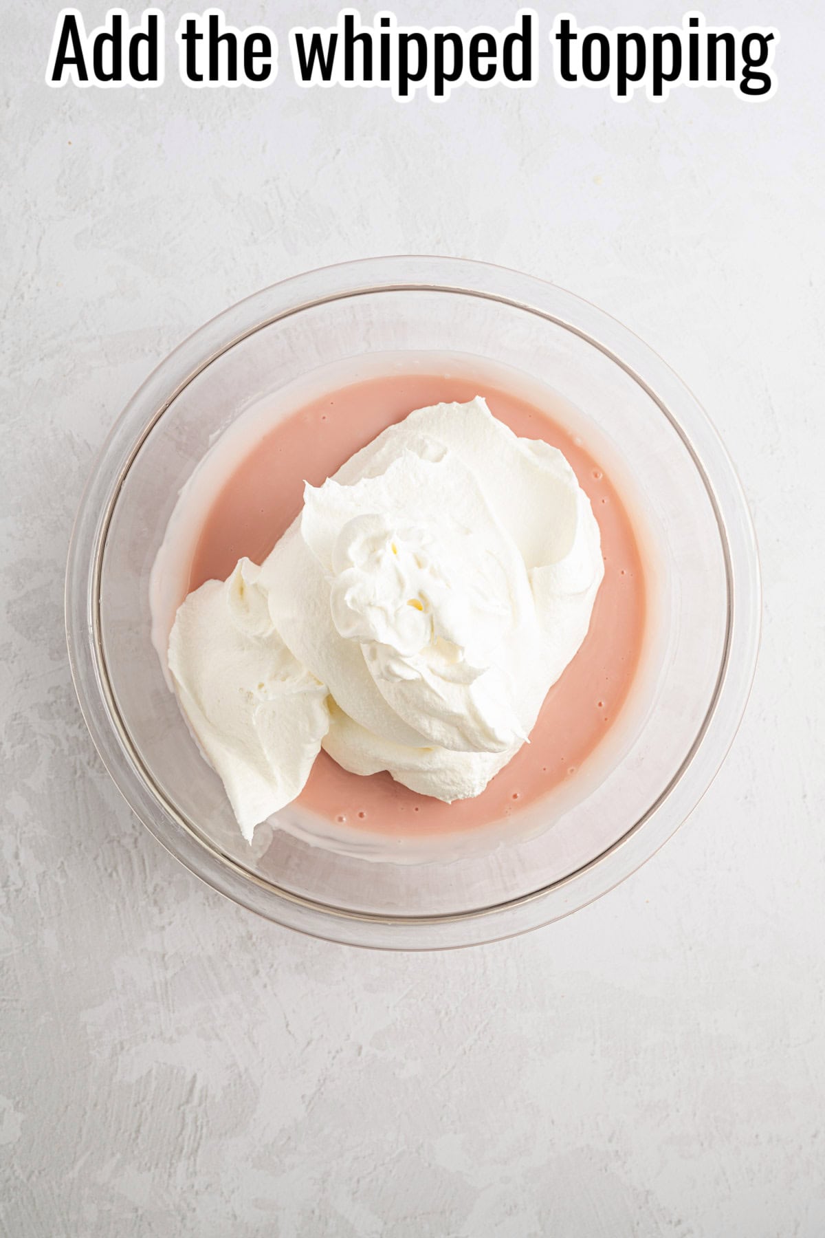 A bowl with whipped topping on top of the creamy mixture. Text on the image says 'Add the whipped topping'.