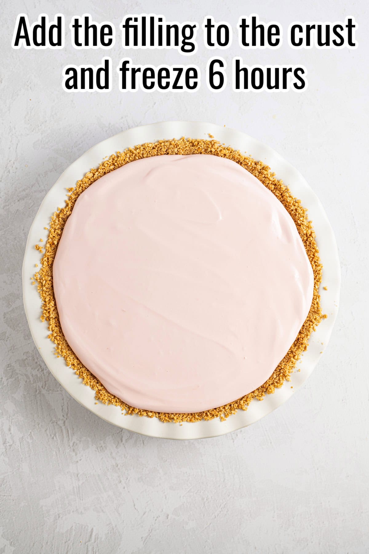 A pink lemonade pie in a white dish with a crumb crust. Text on the image says 'Add the filling to the crust and freeze 6 hours'.