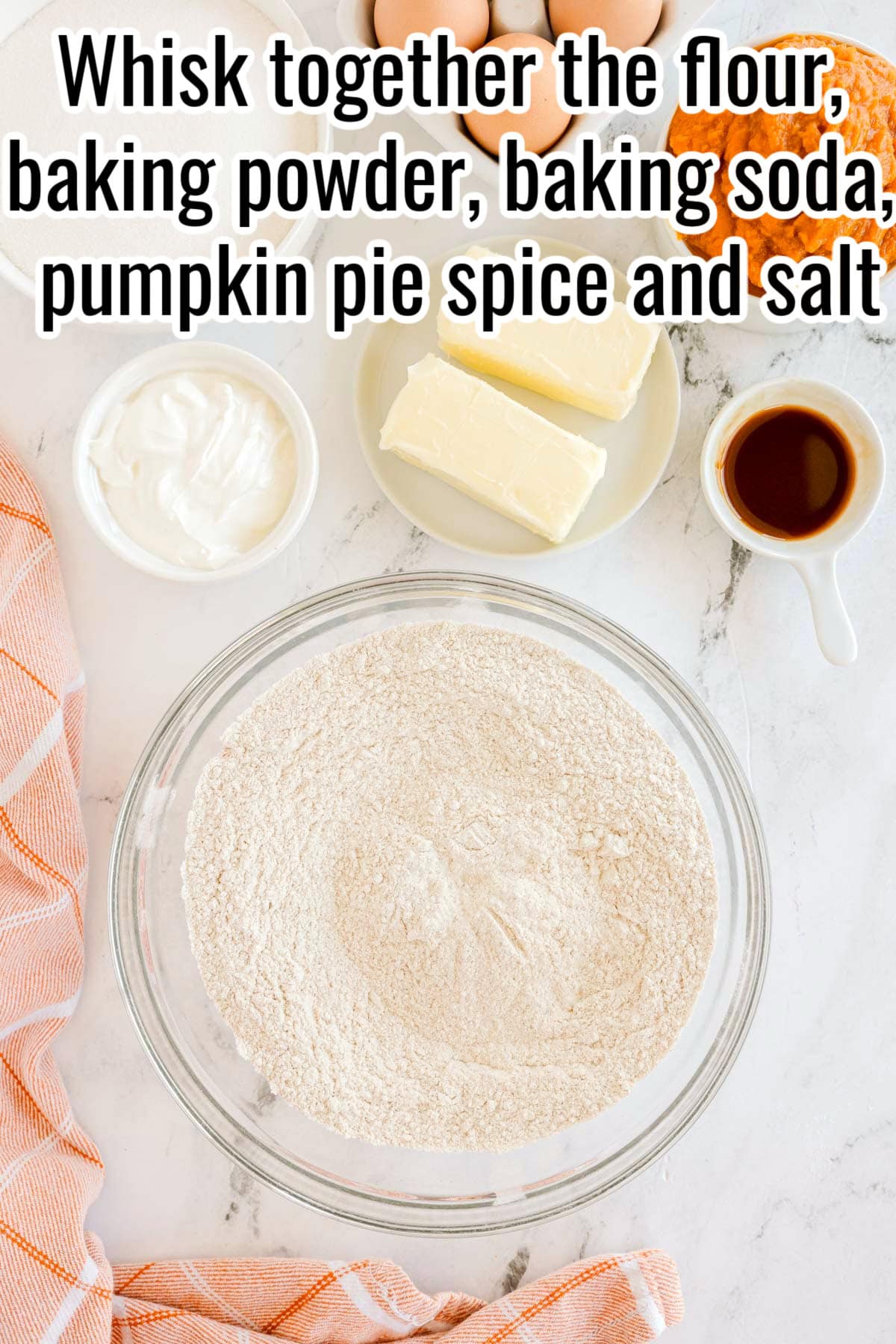 A glass bowl with flour, baking powder, baking soda, pumpkin pie spice, and salt. Text on the image says 'In a large bowl, whisk together flour, baking powder, baking soda, pumpkin pie spice, and salt'.