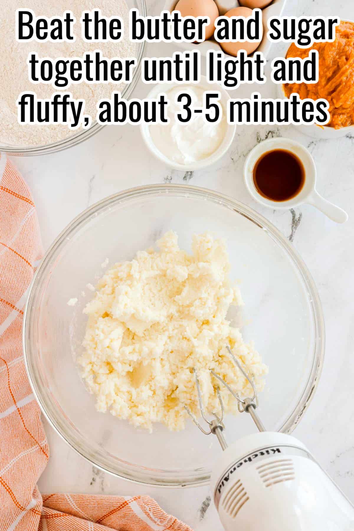 A glass bowl with creamed butter and sugar, with a hand mixer resting inside. Text on the image says "Beat the butter and sugar together until light and fluffy, about 3-5 minutes".