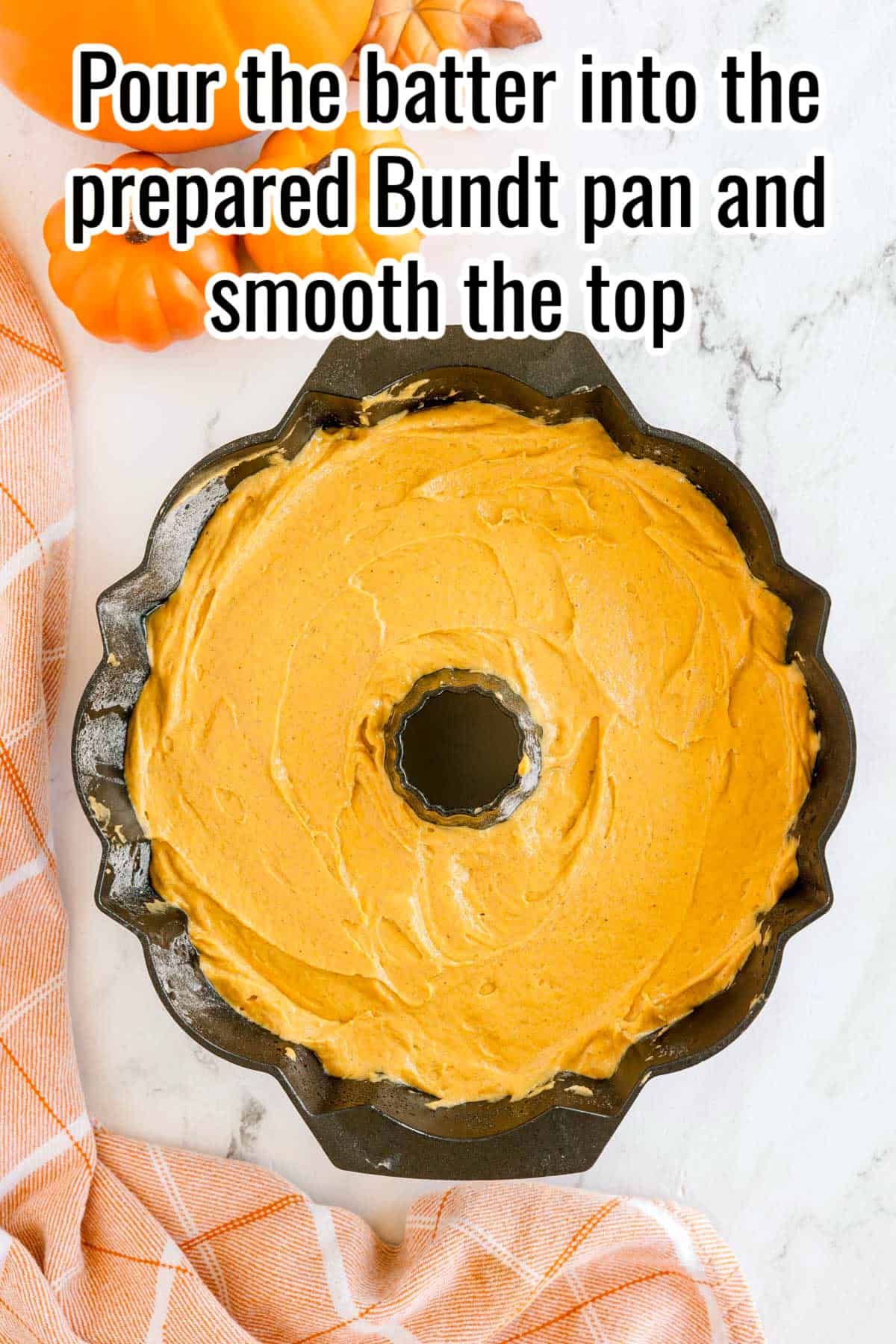 A Bundt pan filled with pumpkin batter on a white countertop. Text on the image says 'Pour the batter into the prepared Bundt pan and smooth the top'.
