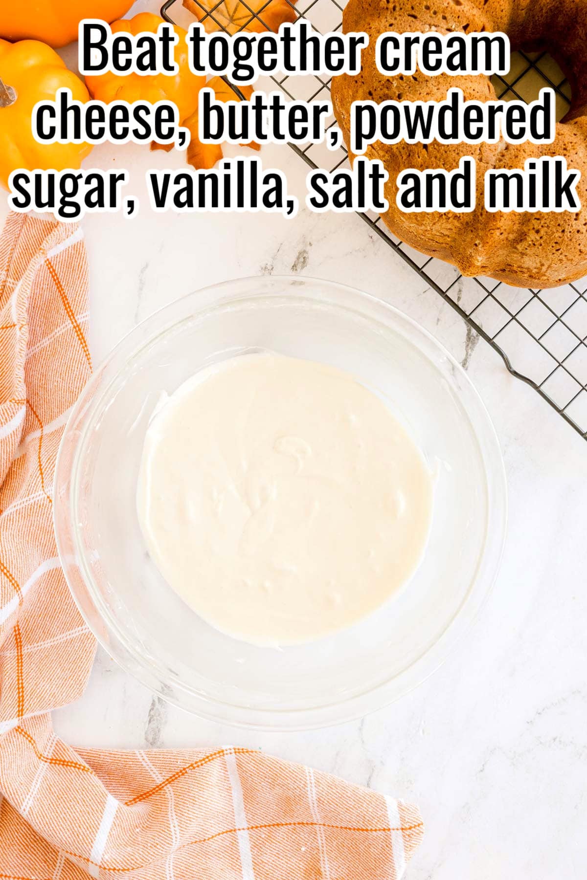 A glass bowl with smooth white frosting. Text on the image says 'Beat together cream cheese, butter, powdered sugar, vanilla, salt and milk'.