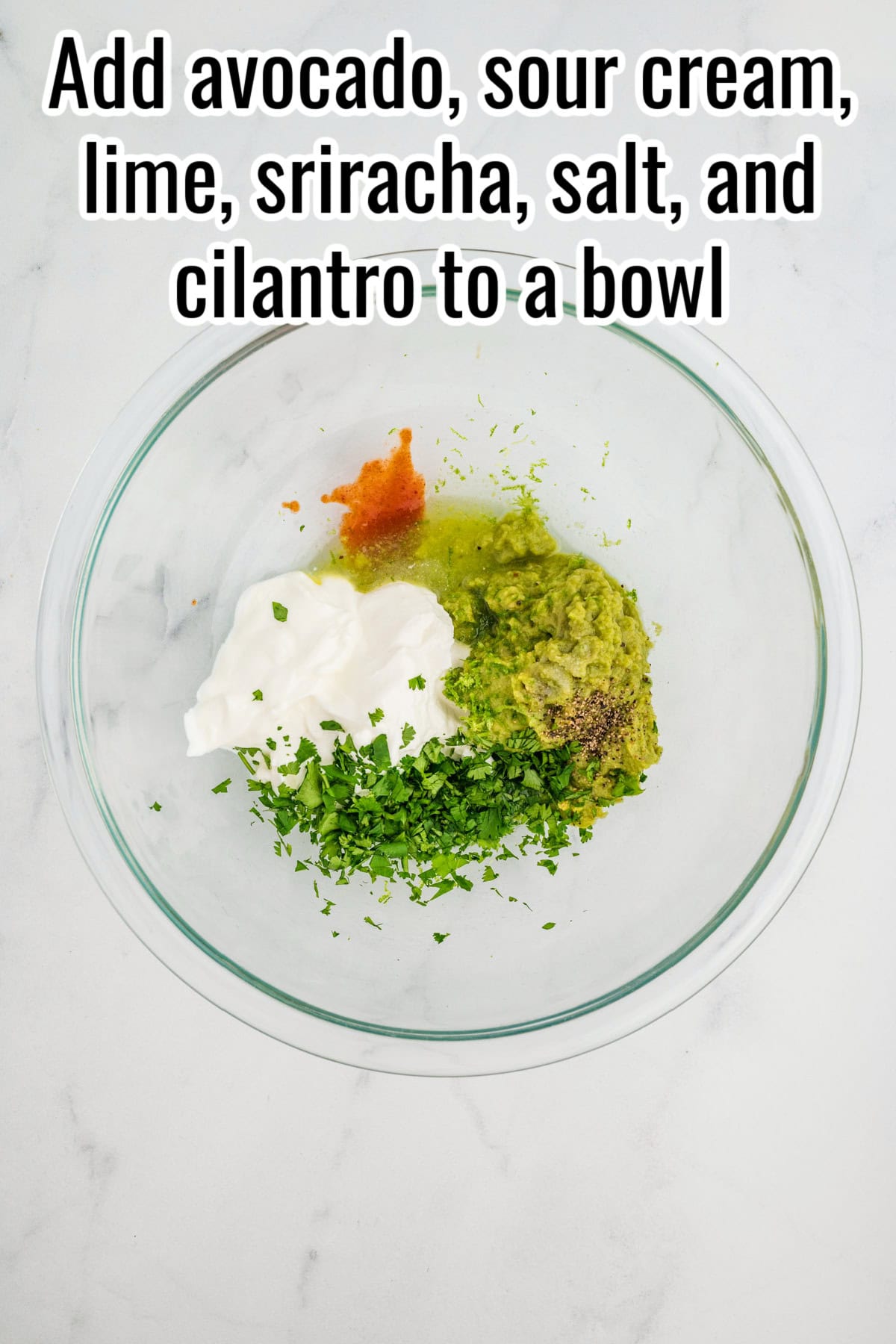 A glass bowl with avocado, sour cream, sriracha, lime juice, chopped cilantro, salt, and pepper. Text on the image says 'Add avocado, sour cream, lime, sriracha, salt, and cilantro to a bowl'.