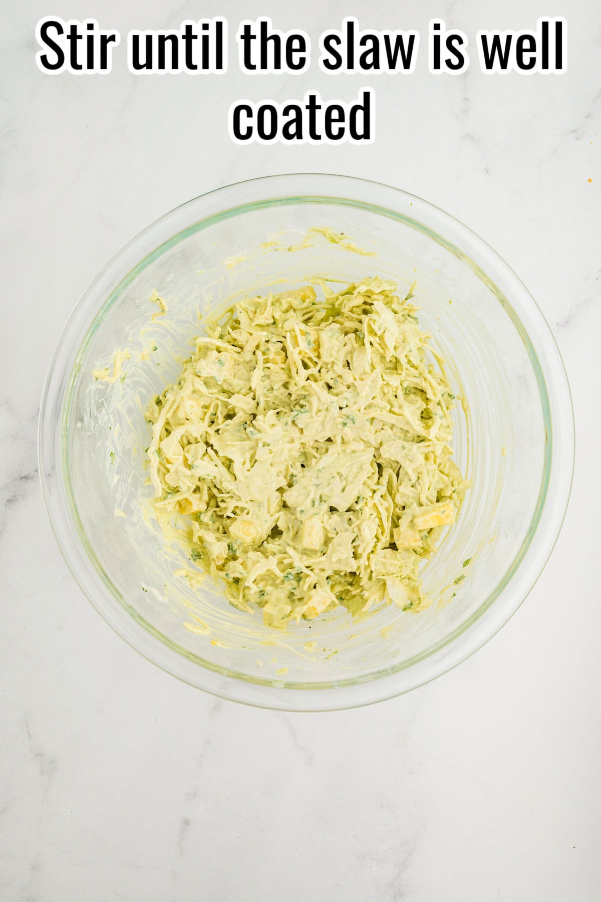 A bowl of cabbage and pineapple slaw coated in avocado dressing. Text on the image says 'Stir until the slaw is well coated'.