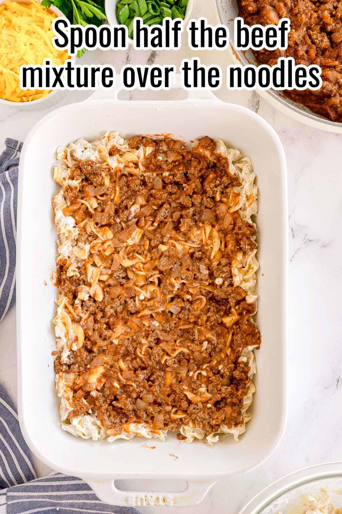 A baking dish with creamy noodles topped with beef mixture. Text on the image says 'Spoon half the beef mixture over the noodles'