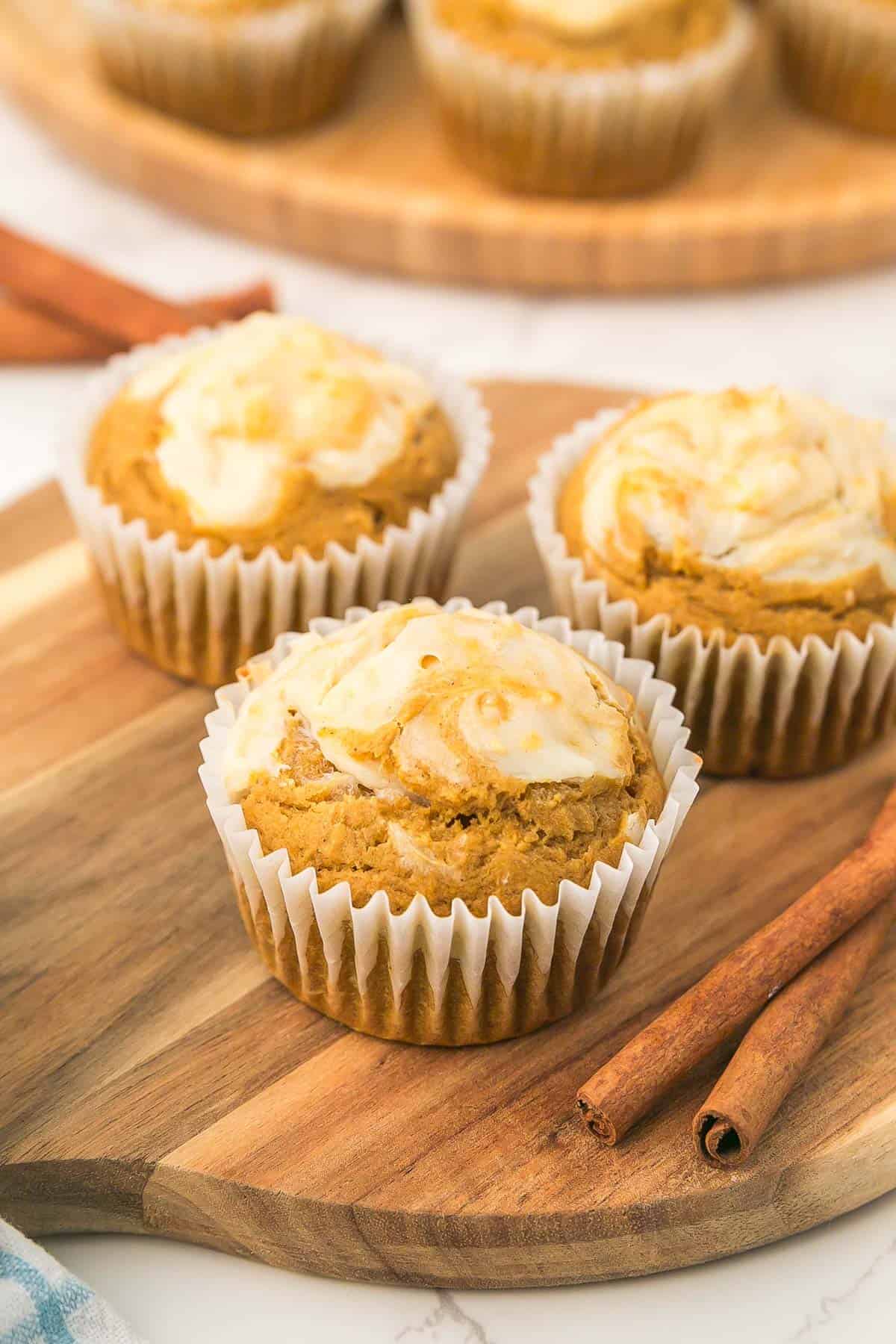 Three pumpkin cream cheese muffins on a wooden board with cinnamon sticks.