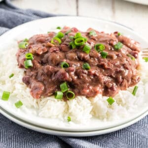 A plate of white rice topped with red beans in sauce, garnished with chopped green onions.