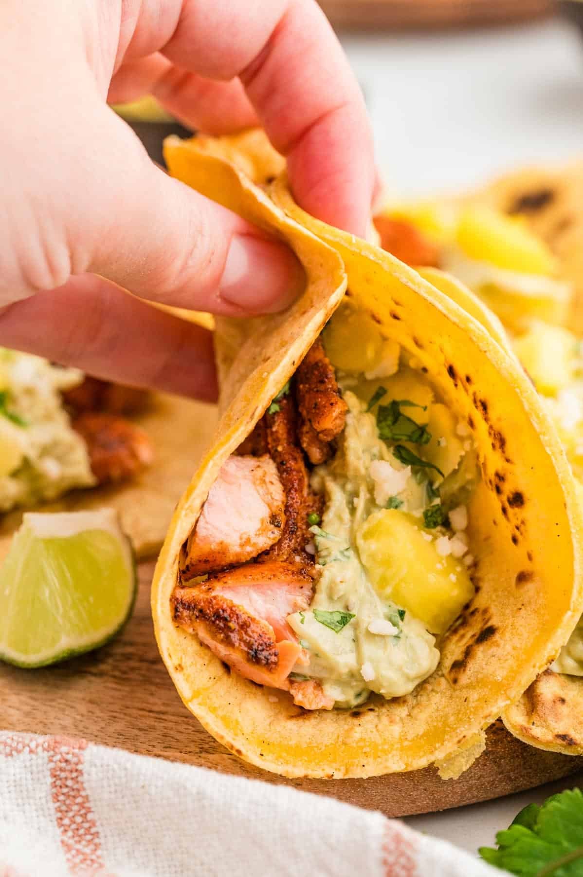 A hand holding a salmon taco filled with pineapple, slaw, and cotija cheese.