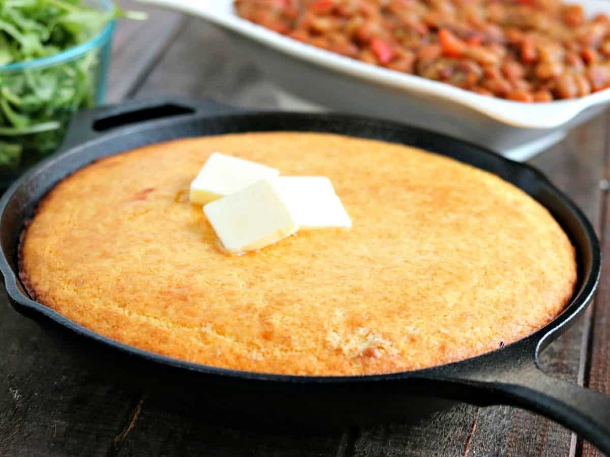 Fluffy and Golden, this Skillet Cornbread is a cinch to make, and is fantastic side for any meal! cast iron skillet of cornbread with butter on top